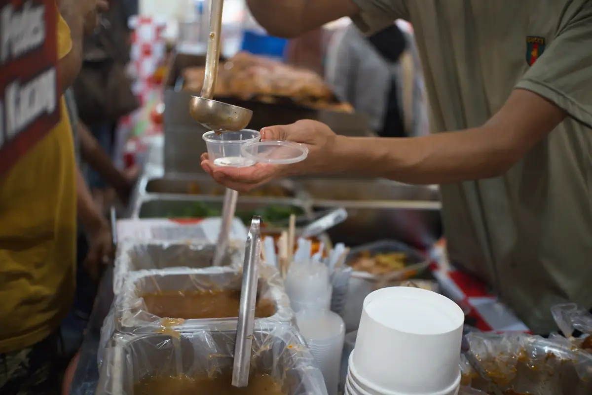 A cook ladling broth into a small container at a market stall