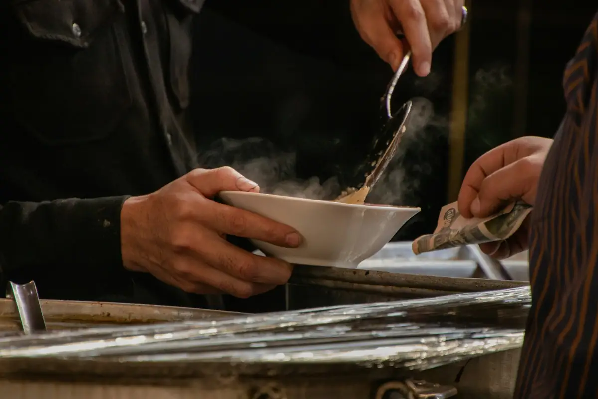 Hands ladling a stew into a bowl in a dim kitchen