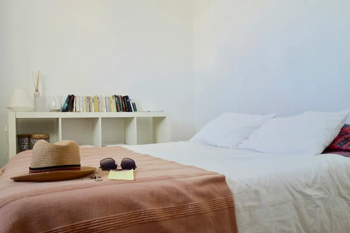 A white bedroom with a straw hat and sunglasses left on the bed