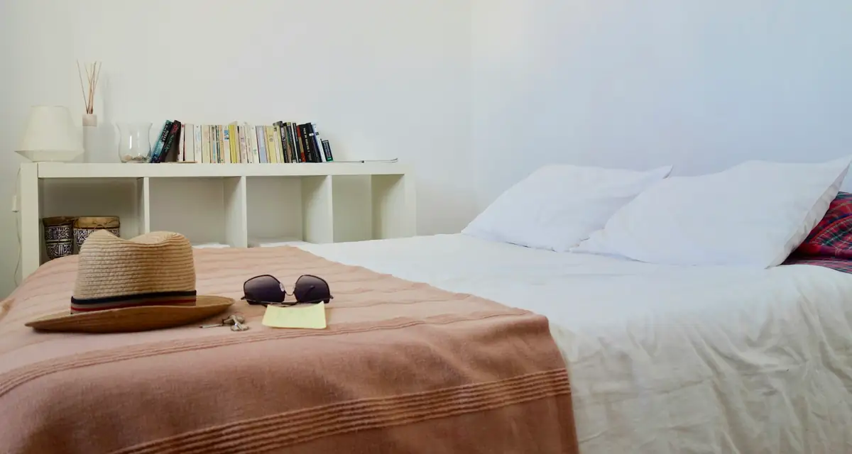 A white bedroom with a straw hat and sunglasses left on the bed