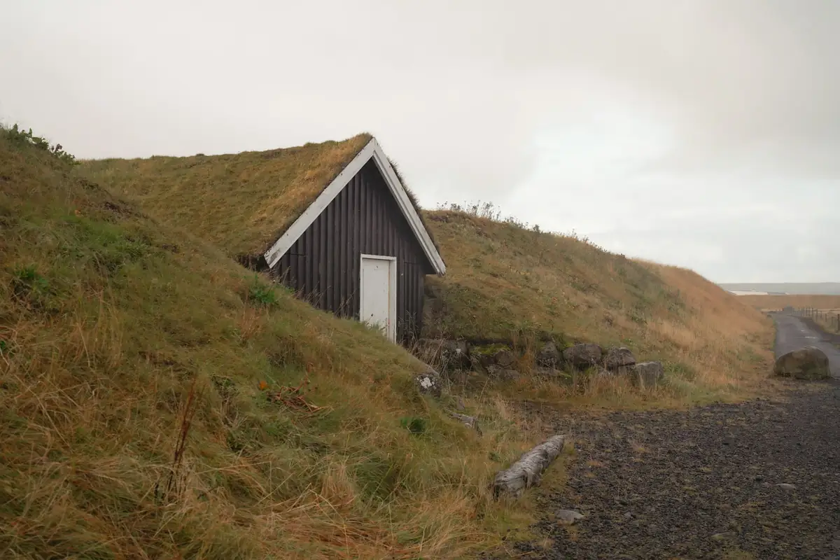 A small turf-roofed house set into a grass bank near the shore