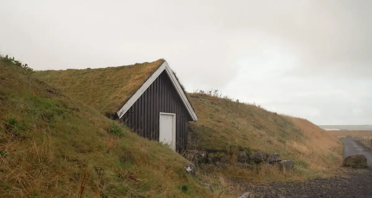 A small turf-roofed house set into a grass bank near the shore