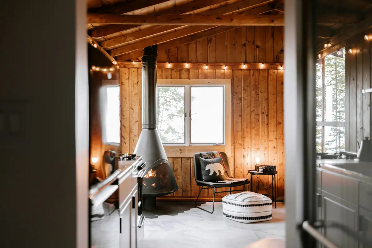 A timber-lined room with a black wood stove and strung lights