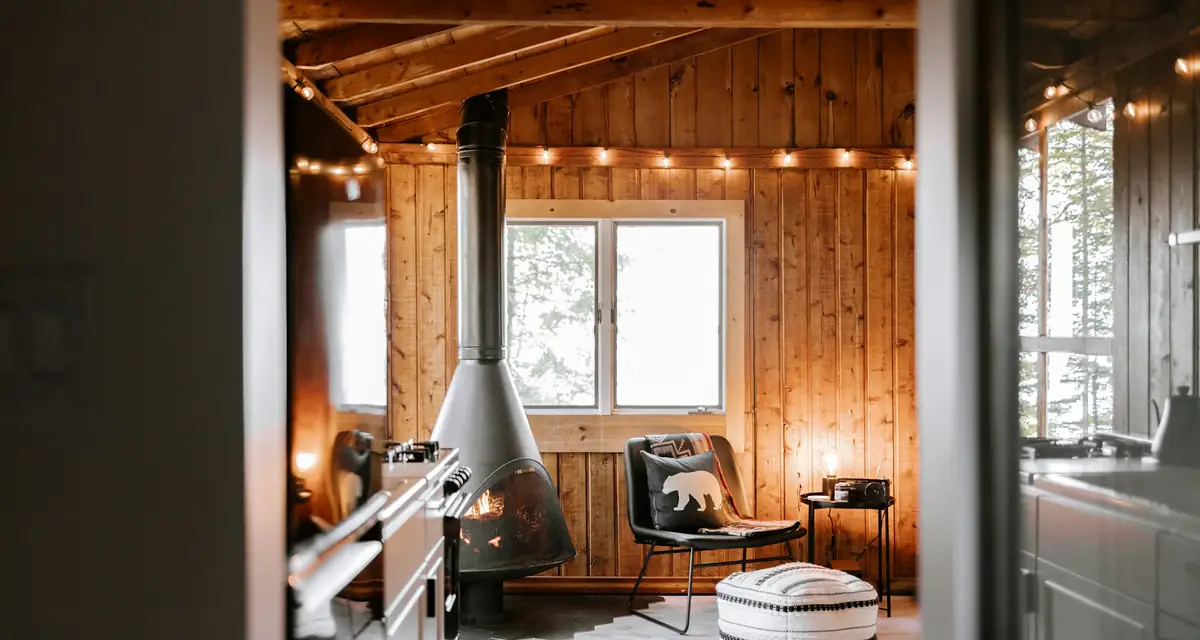 A timber-lined room with a black wood stove and strung lights